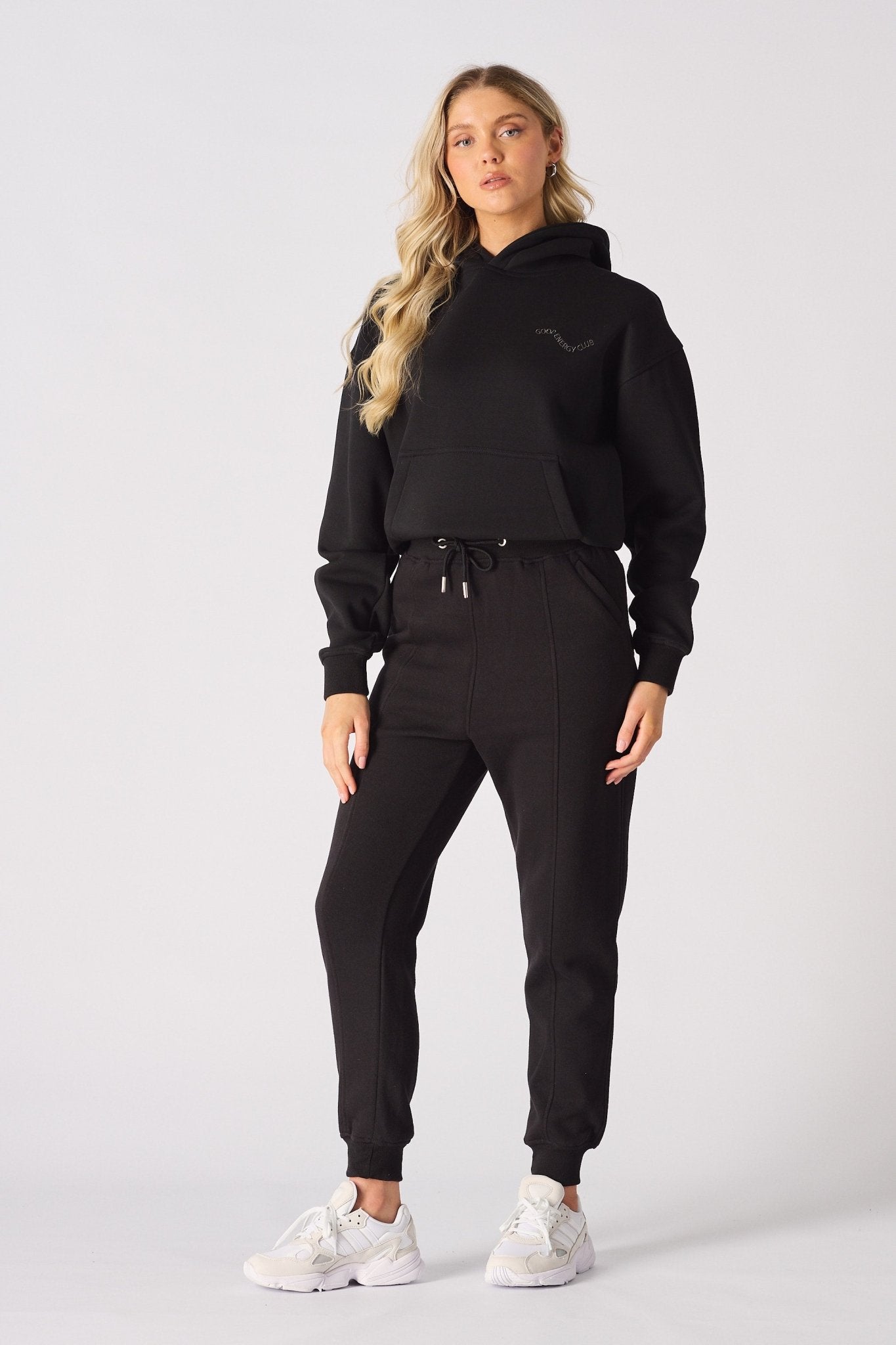 Full body view of a model posing in black tapered joggers womens and trainers.