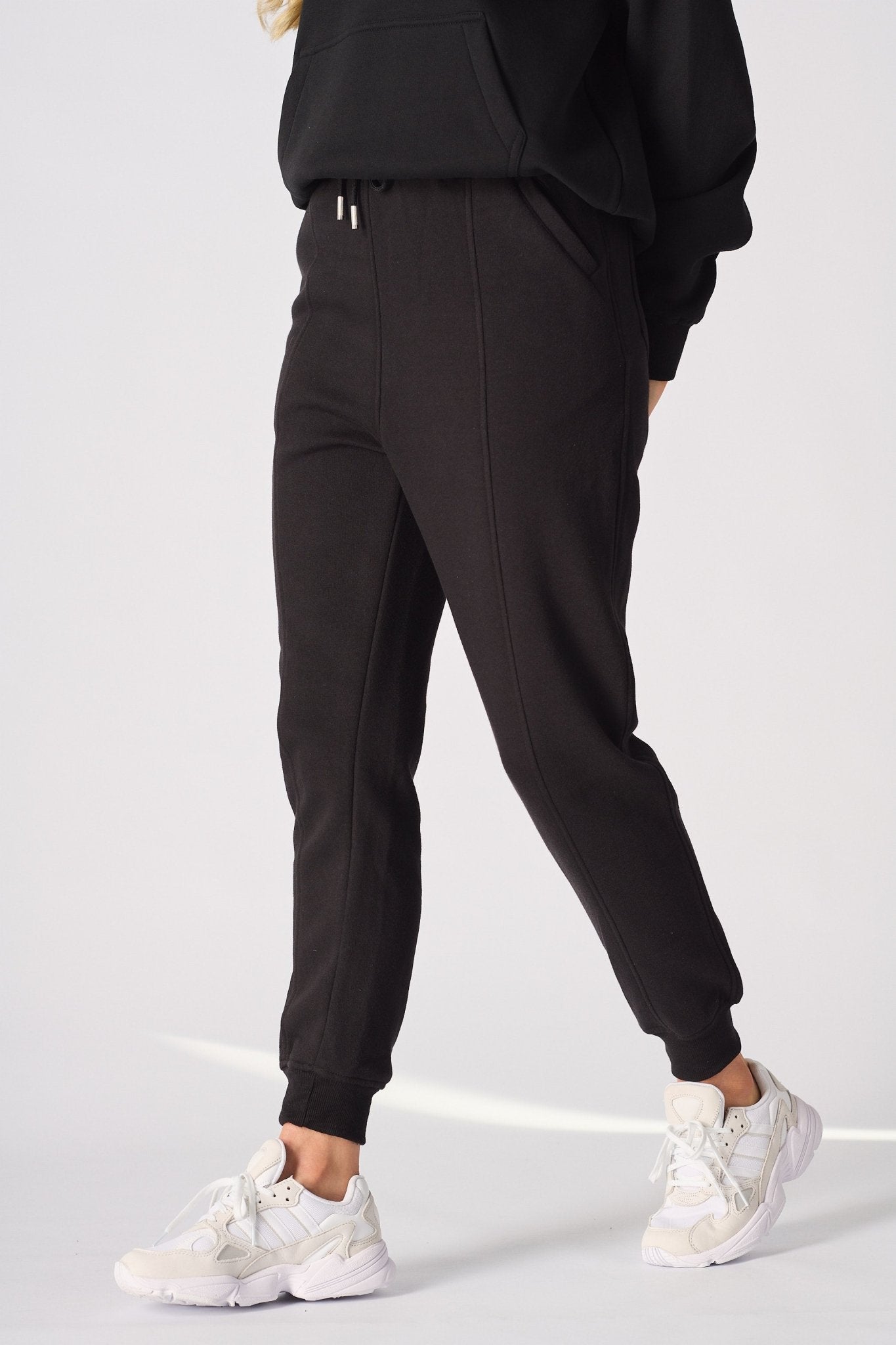Side angle of a model walking in high quality black tapered joggers womens.