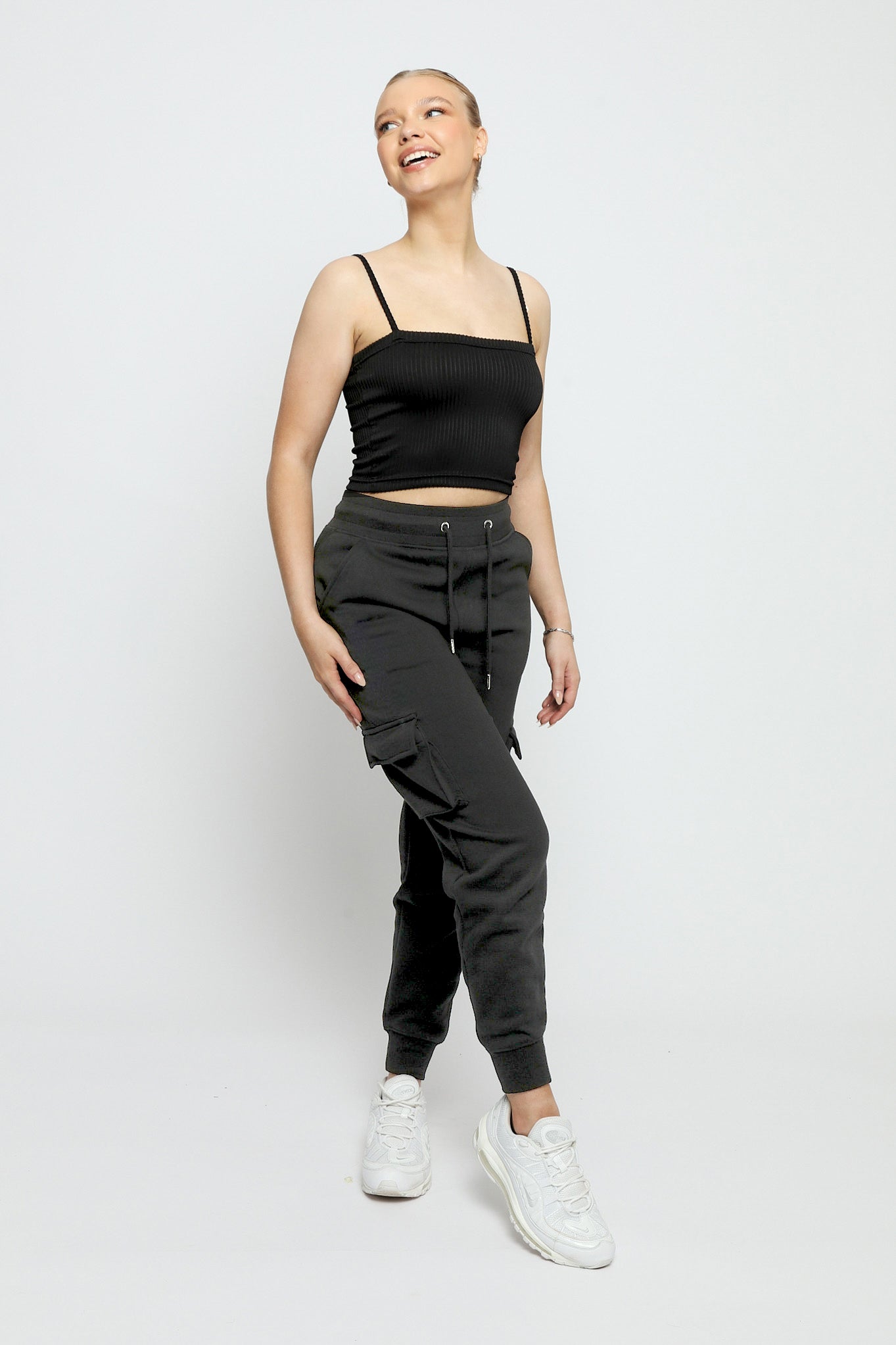 Full length shot of a woman wearing black utility joggers womens and white trainers.