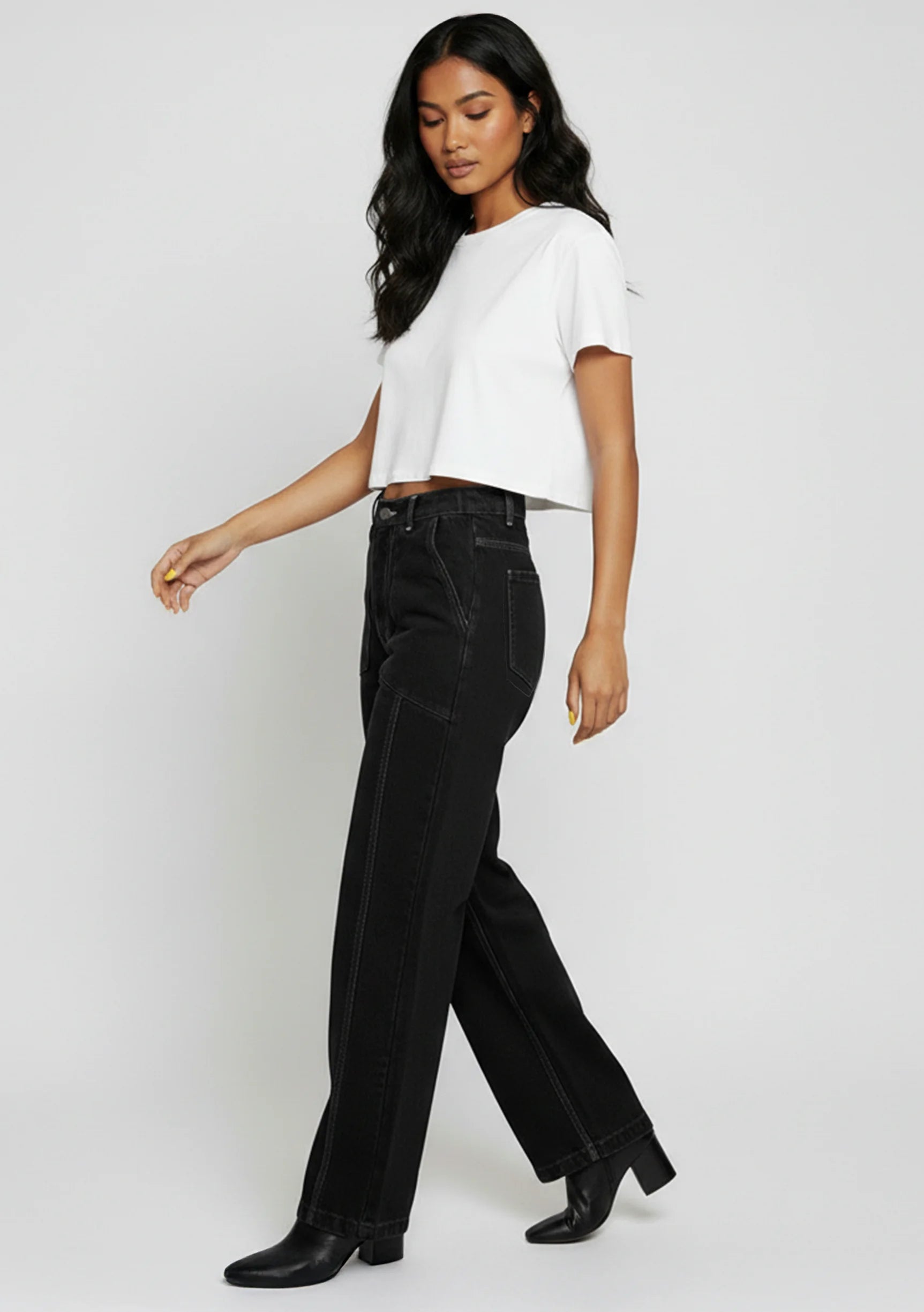 Model walking in high-waist black wide-leg jeans showing the side drape and movement.