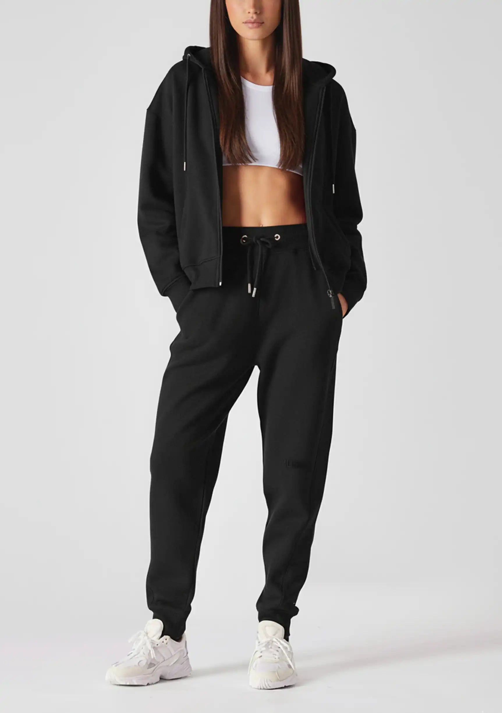 A woman wearing a premium black zip up hoodie womens with matching joggers and white trainers.