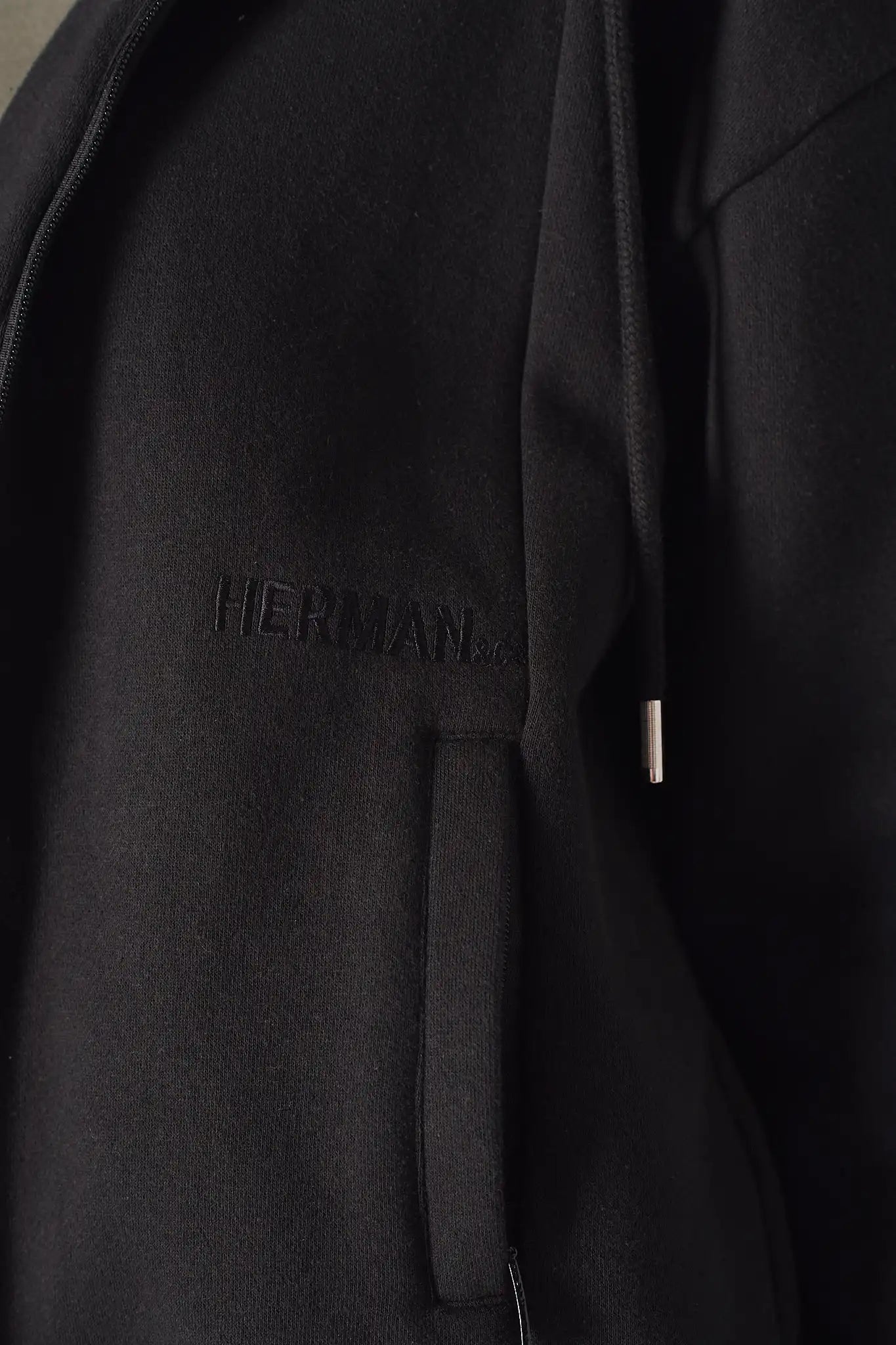 Close up showing the discreet tonal embroidery and pocket on the black zip up hoodie womens.