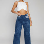 Front view of women's blue acid wash wide leg jeans with embellished pockets and slit hems