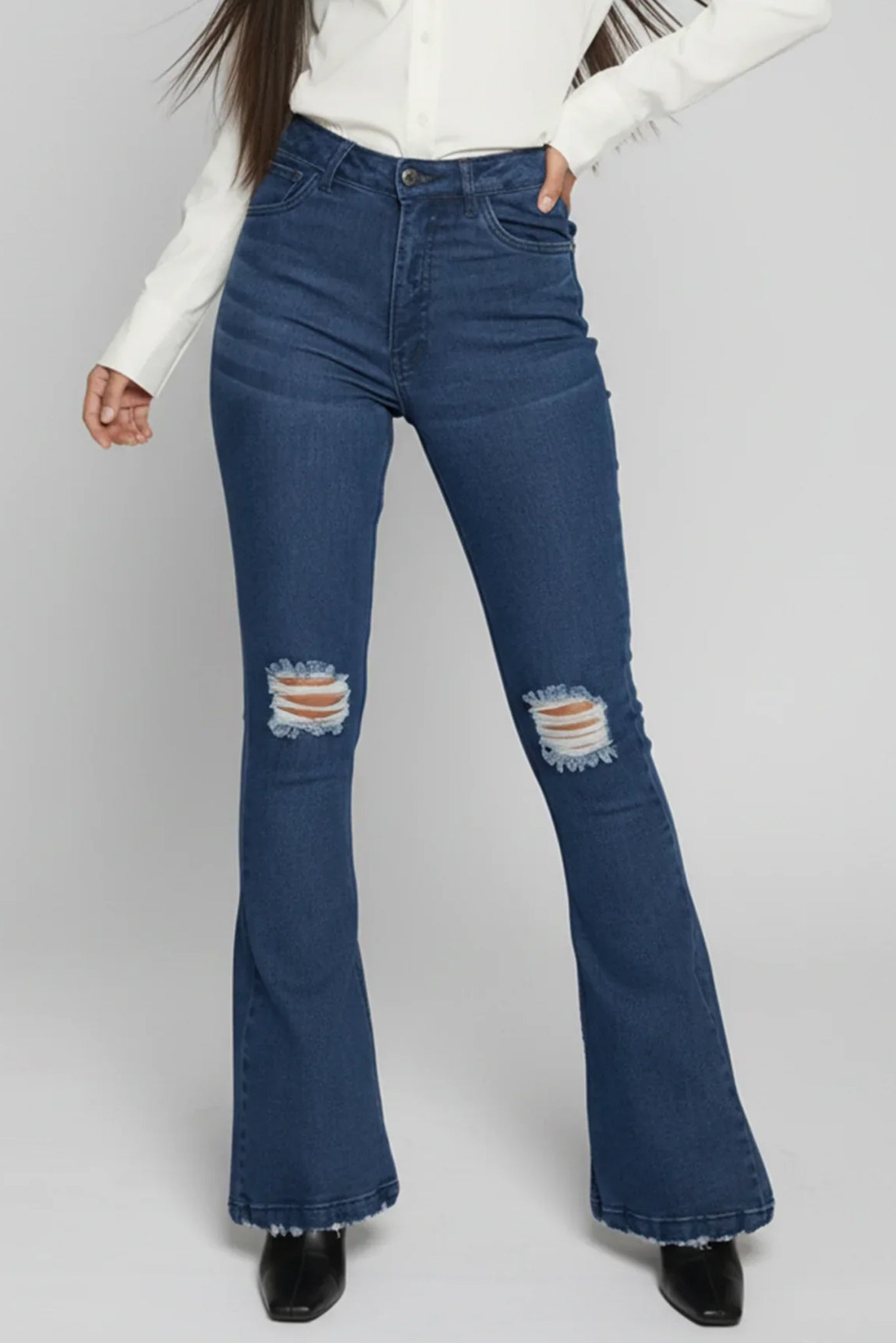 Blue flared jeans with distressed details worn by a person on a white background