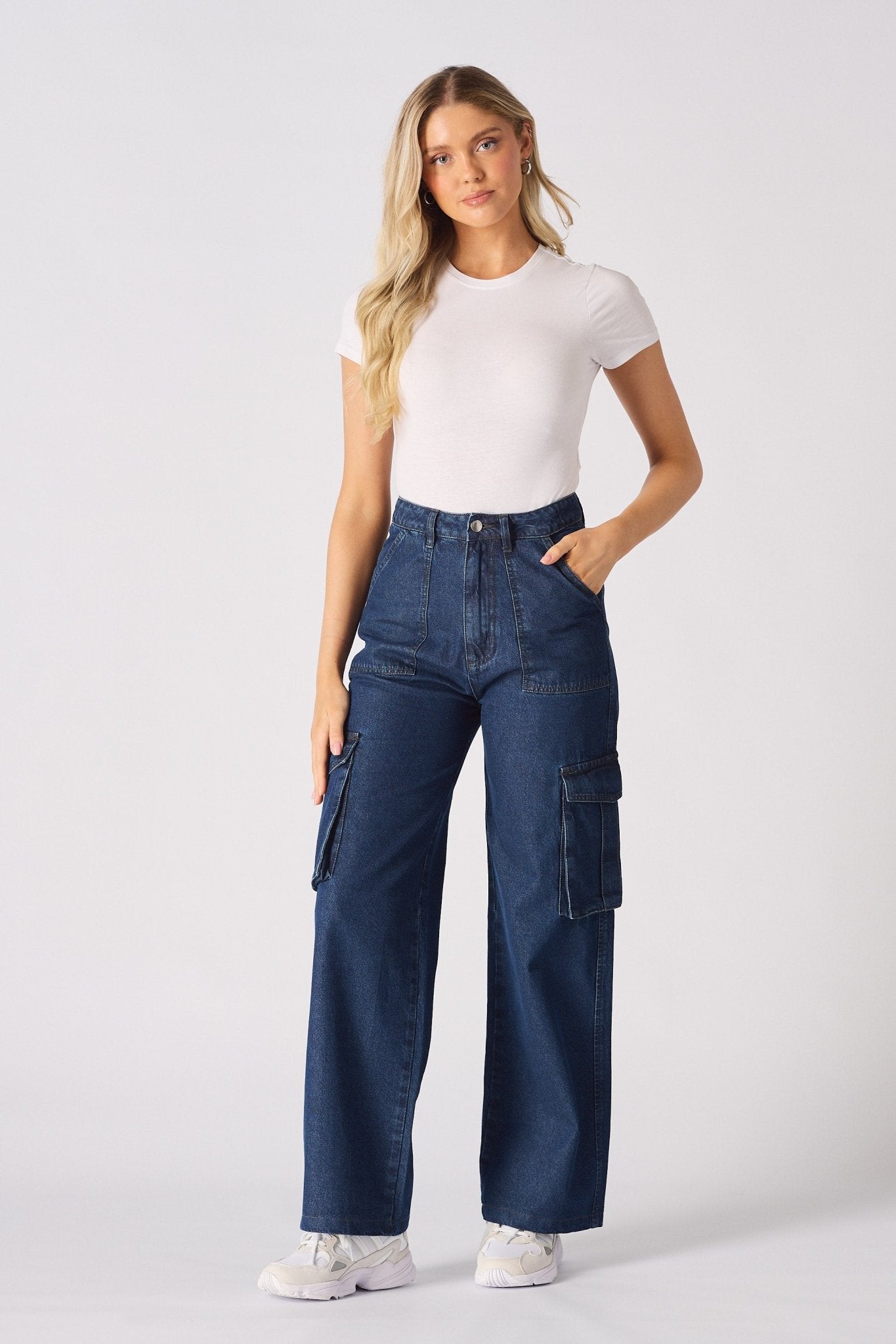 A model posing in blue high waisted wide leg cargo denim jeans women with her hands on the waistband.