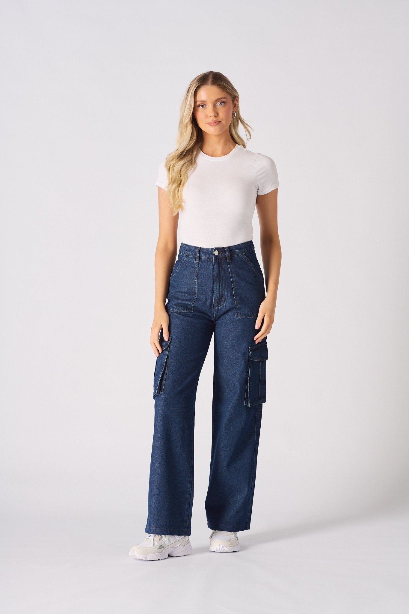 A full length front view of the blue high waisted wide leg cargo denim jeans women with white trainers.