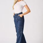 Side view of a woman wearing blue high waisted wide leg cargo denim jeans women styled with white trainers.