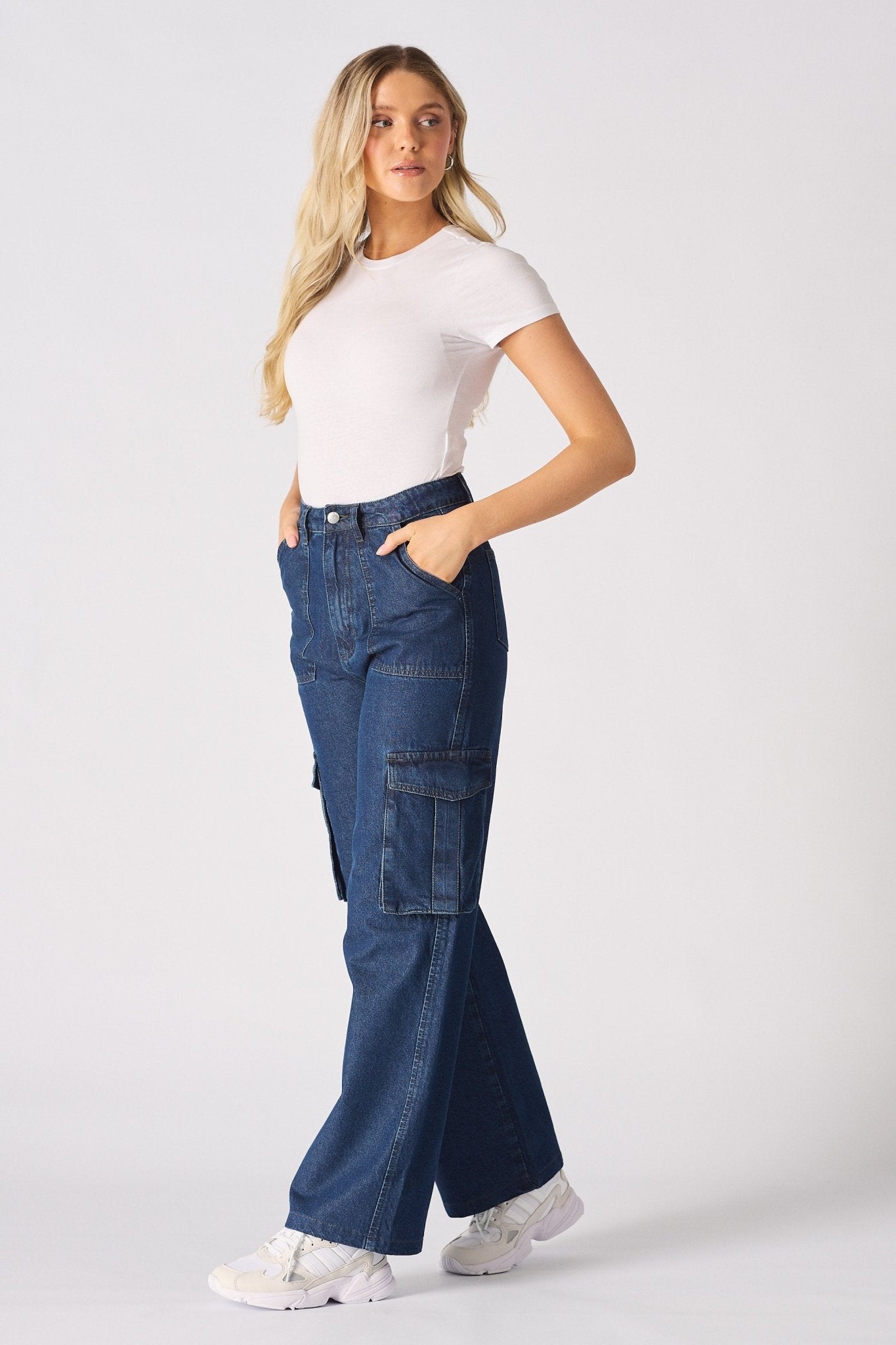 Side view of a woman wearing blue high waisted wide leg cargo denim jeans women styled with white trainers.