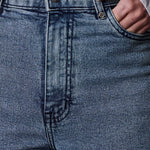 Close-up of blue jeans with a hand in the pocket, wearing a white shirt.
