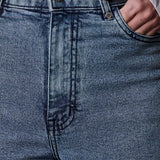 Close-up of blue jeans with a hand in the pocket, wearing a white shirt.