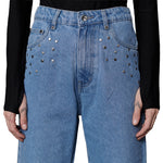 Blue jeans with decorative studs worn by a person against a black background