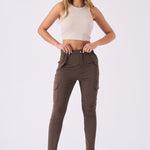 A woman posing in high waisted brown skinny cargo jeans with a beige top and clear heels.