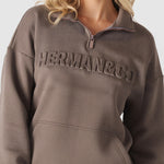 Close up showing the embossed logo detail on the brown quarter zip sweatshirt.