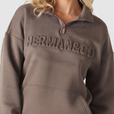 Close up showing the embossed logo detail on the brown quarter zip sweatshirt.