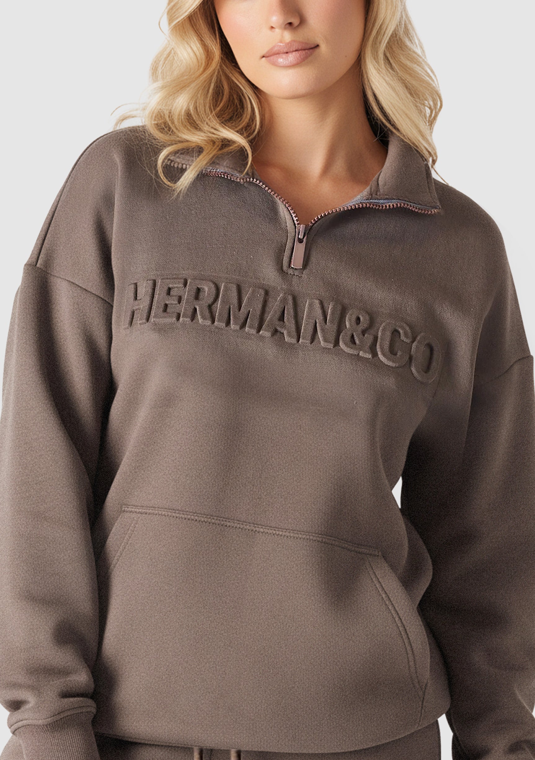 Close up showing the embossed logo detail on the brown quarter zip sweatshirt.