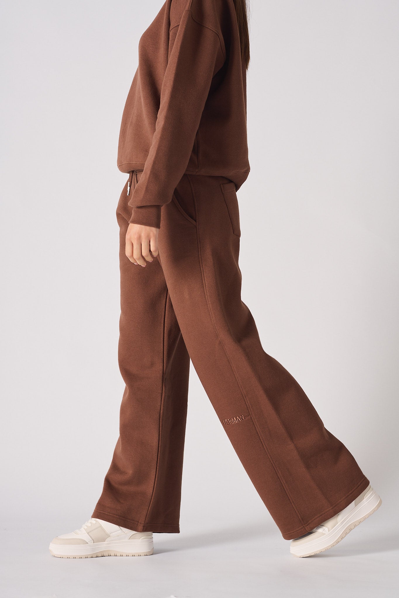 Side view of a woman walking in chocolate brown wide leg joggers and a matching jumper