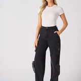 A woman posing in high-waisted black cargo jeans paired with a white t-shirt and white trainers.