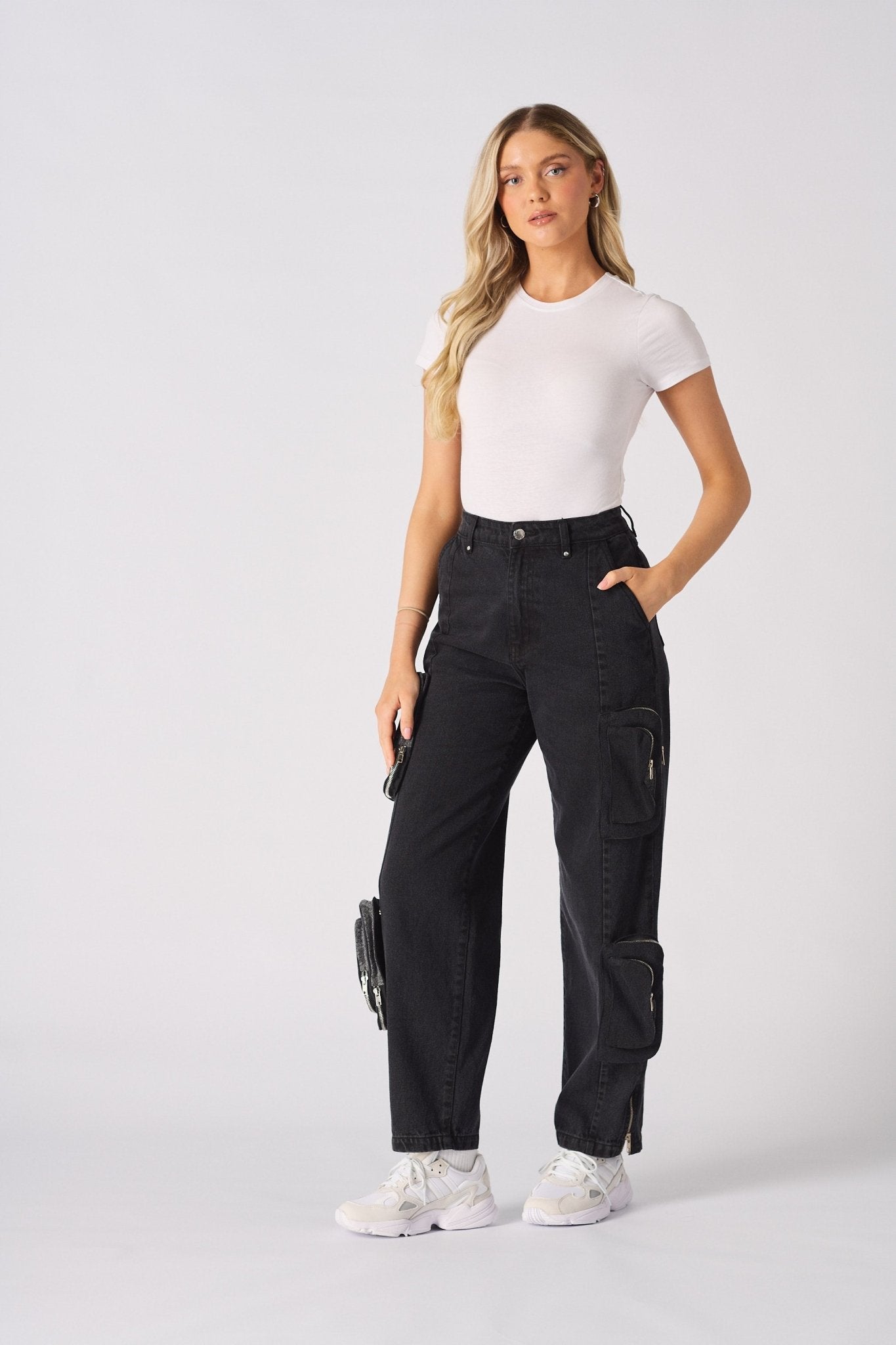 A woman posing in high-waisted black cargo jeans paired with a white t-shirt and white trainers.