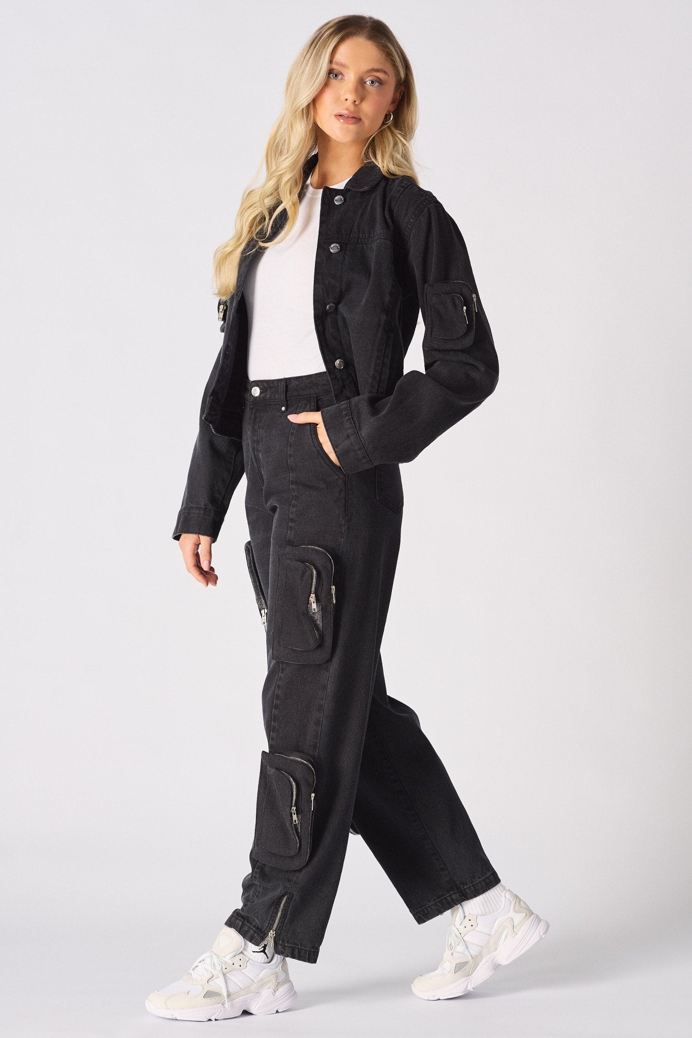 A model wearing black cargo jeans for women with a matching denim jacket and white trainers.