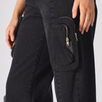 A zoomed in view of the multiple zip on utility pockets on the black denim fabric.