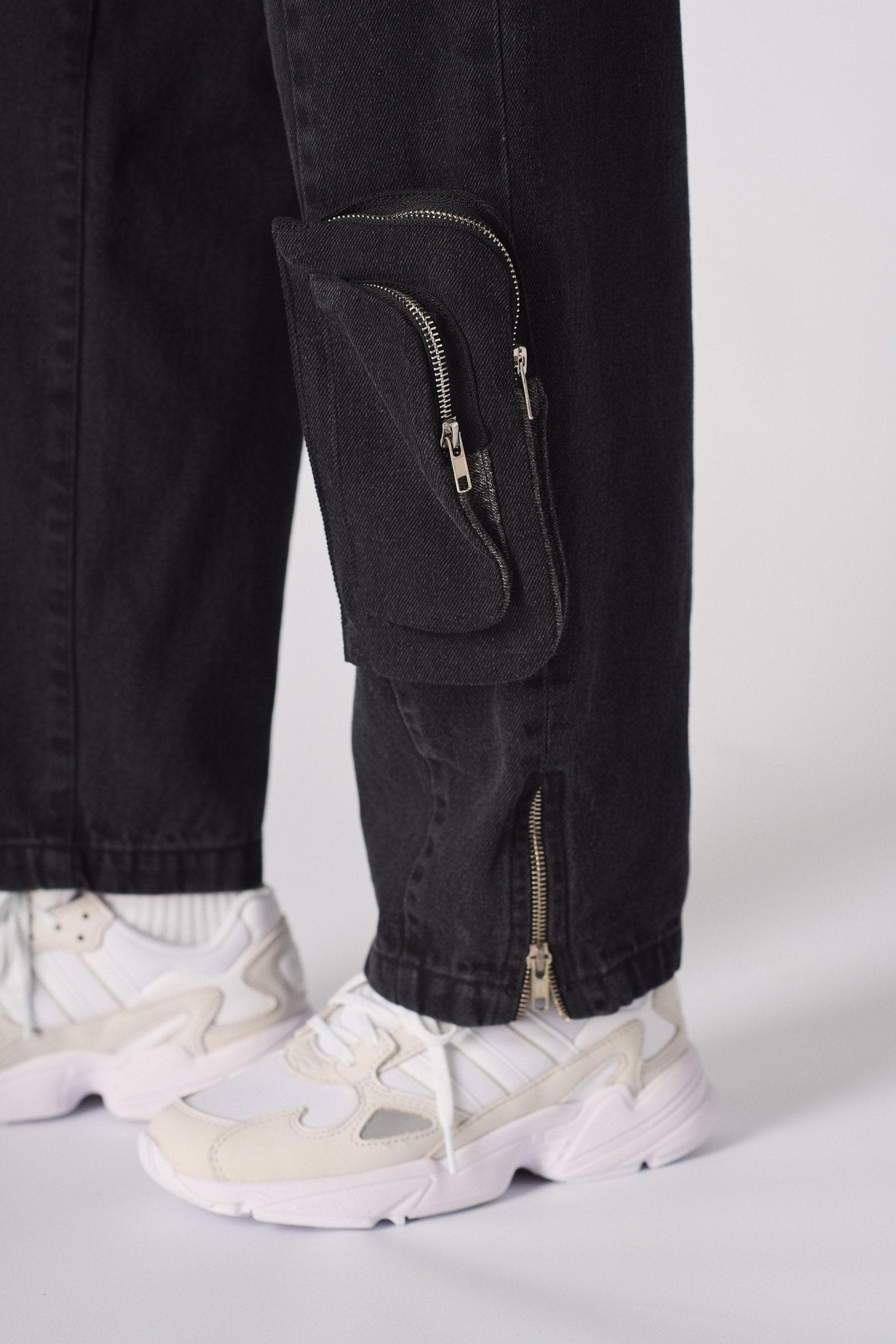 Detailed shot of the utility pocket and unique zip system on the black cargo jeans.