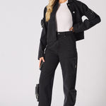 Side view of a woman wearing straight-leg black cargo jeans with functional leg pockets.