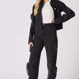 Side view of a woman wearing straight-leg black cargo jeans with functional leg pockets.