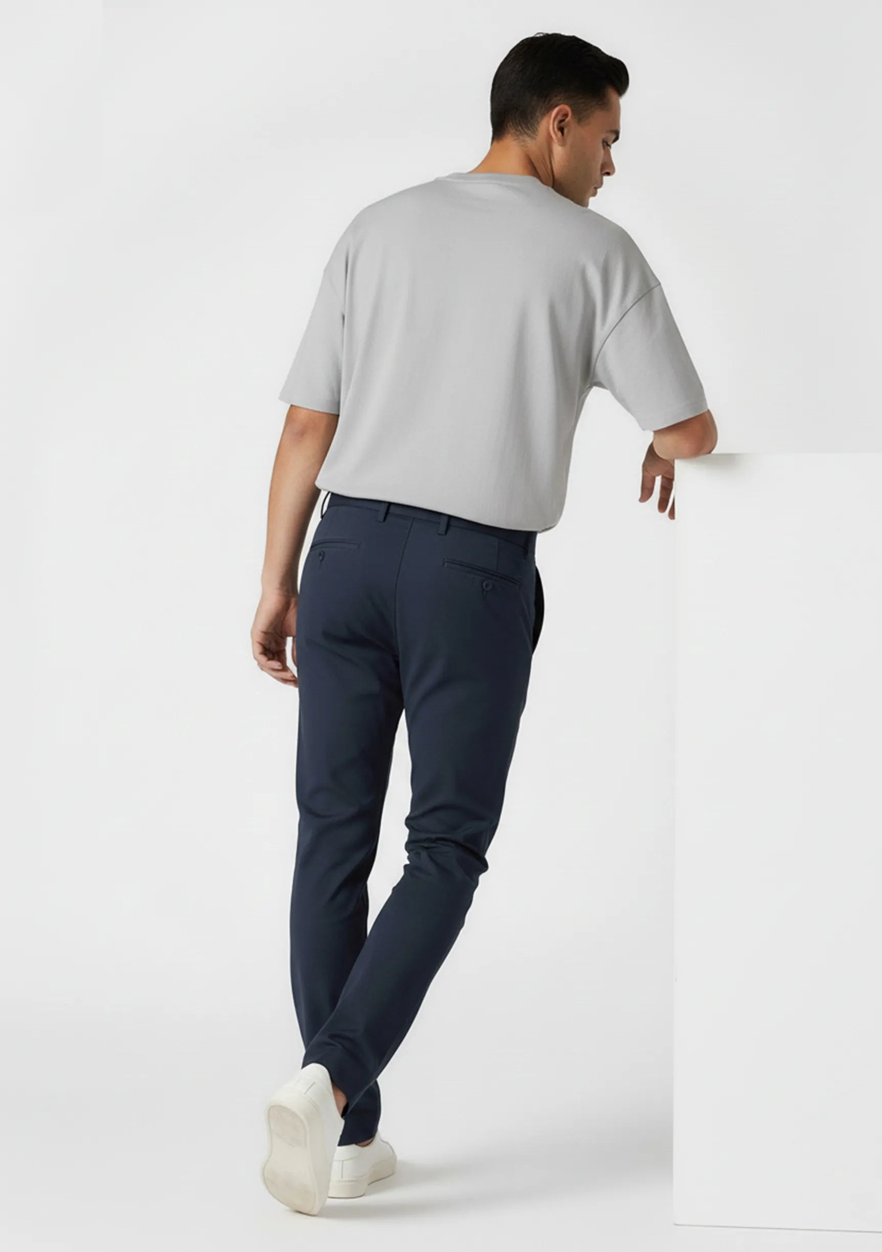 Man leaning against a white block wearing stylish casual blue chinos.