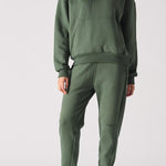 Full front view of a woman posing in a dark green hoodie with matching trousers