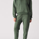 Full front view of a woman posing in a dark green hoodie with matching trousers