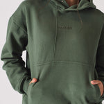 Close up shot of hands in the front pocket of a dark green hoodie for women