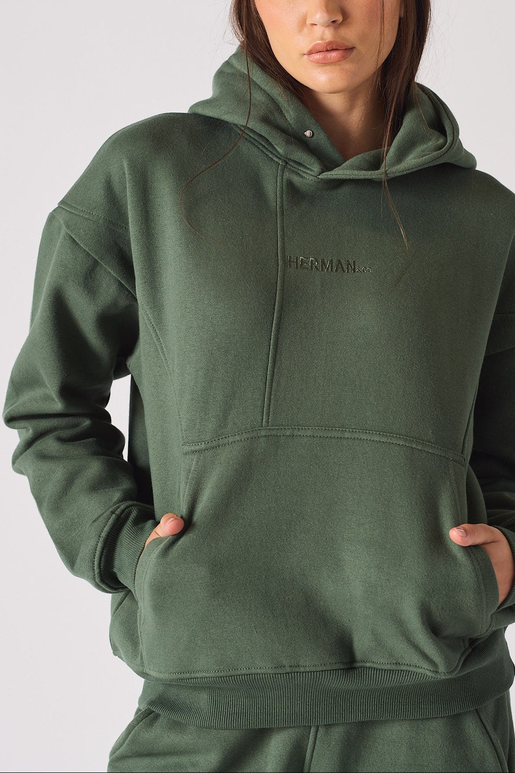 Close up shot of hands in the front pocket of a dark green hoodie for women