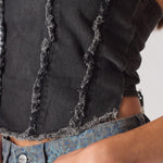 Extreme close up of black corset top showing distressed frayed stitching detail and raw edge texture - women's denim bustier fabric detail