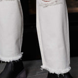 Close-up of the frayed hem and distressed knee detail on the off-white jeans.