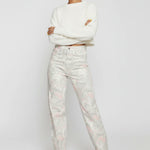 Model standing with arms crossed wearing female swirl wash tapered leg jeans in a light grey tone.