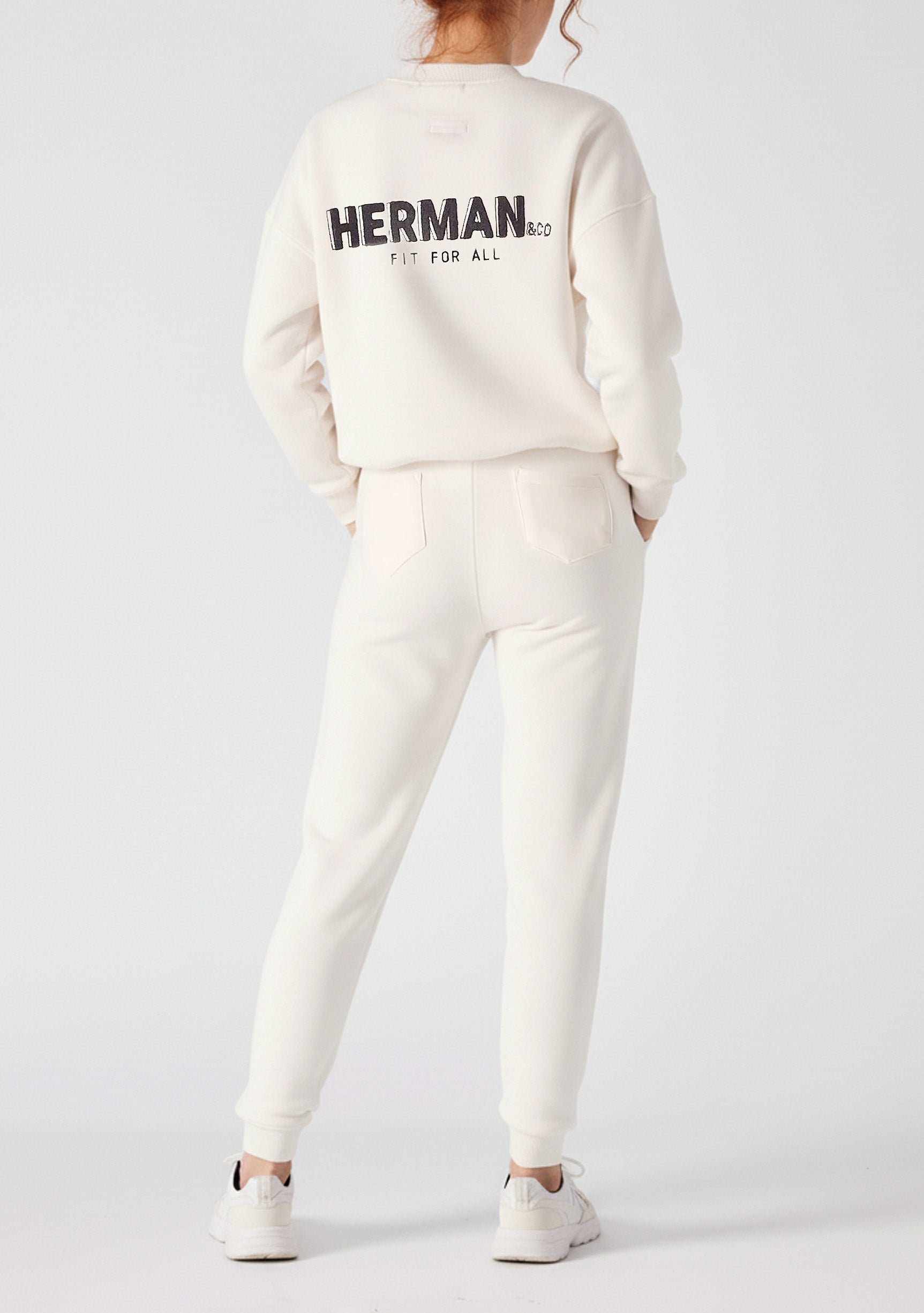 Back view of a woman wearing female white sweatpants and a matching hoodie with a logo.