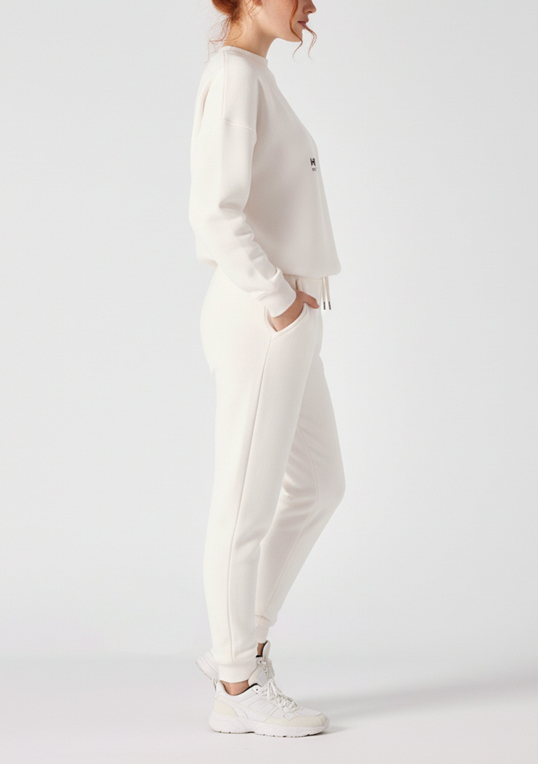 Side view of a woman posing in the relaxed fit female white sweatpants.