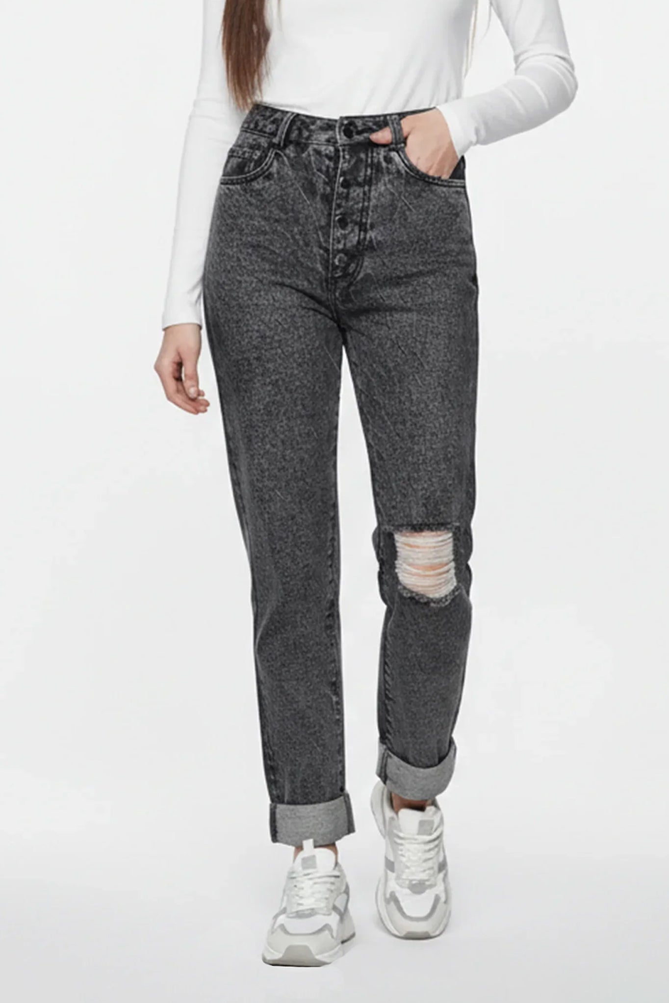 Person wearing gray distressed jeans and white sneakers on a white background