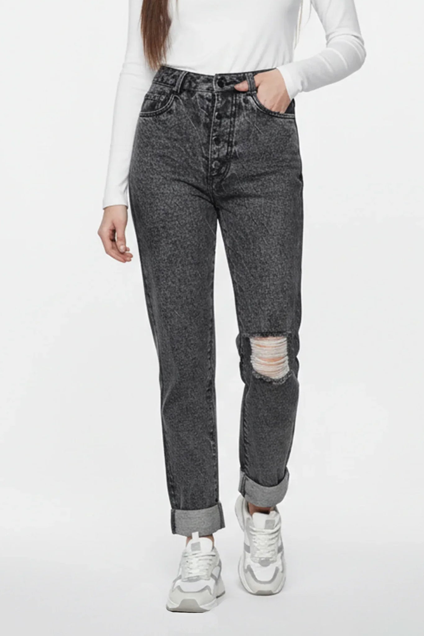 Person wearing gray distressed jeans and white sneakers on a white background