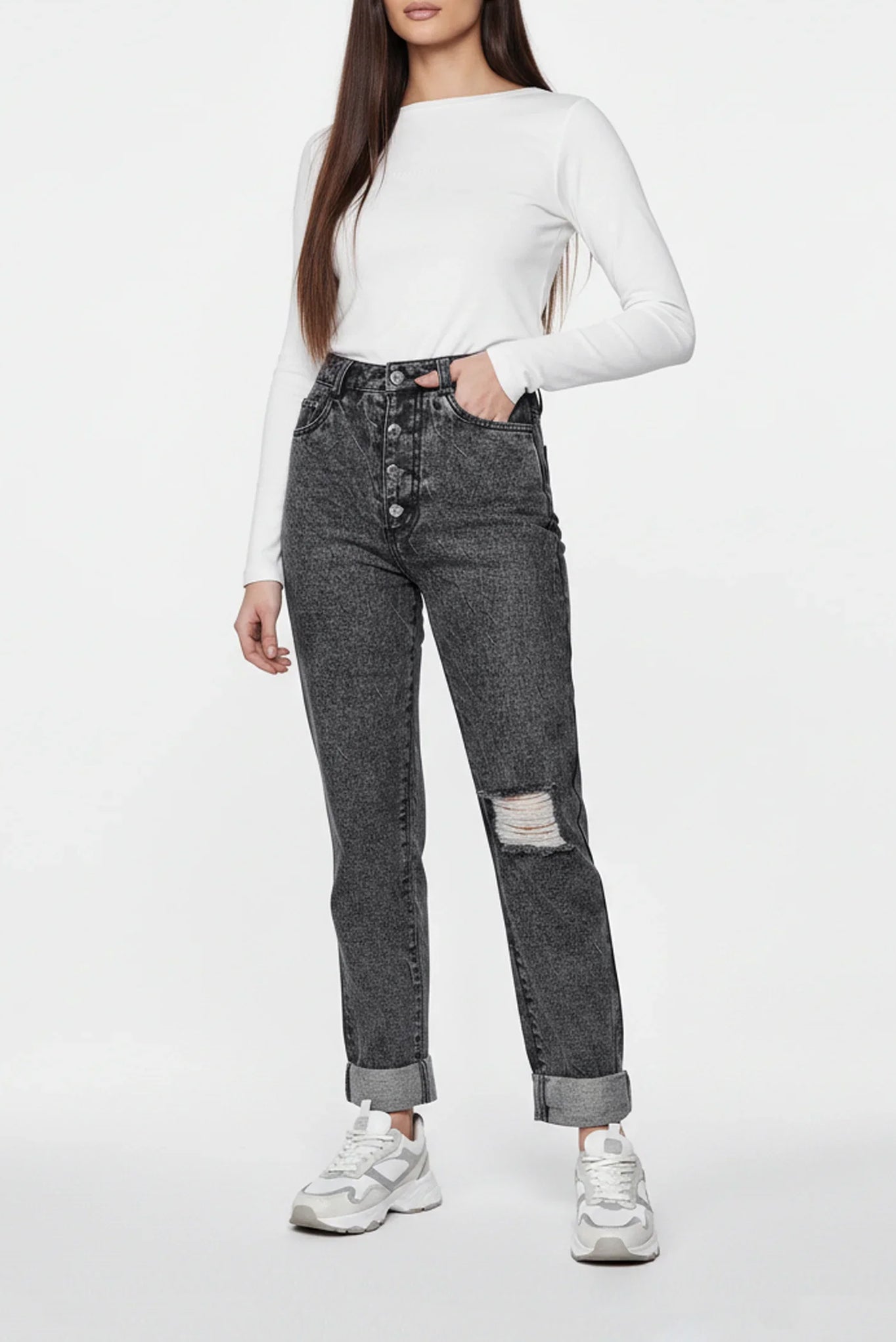 Person wearing a white long-sleeve top and gray distressed jeans on a white background