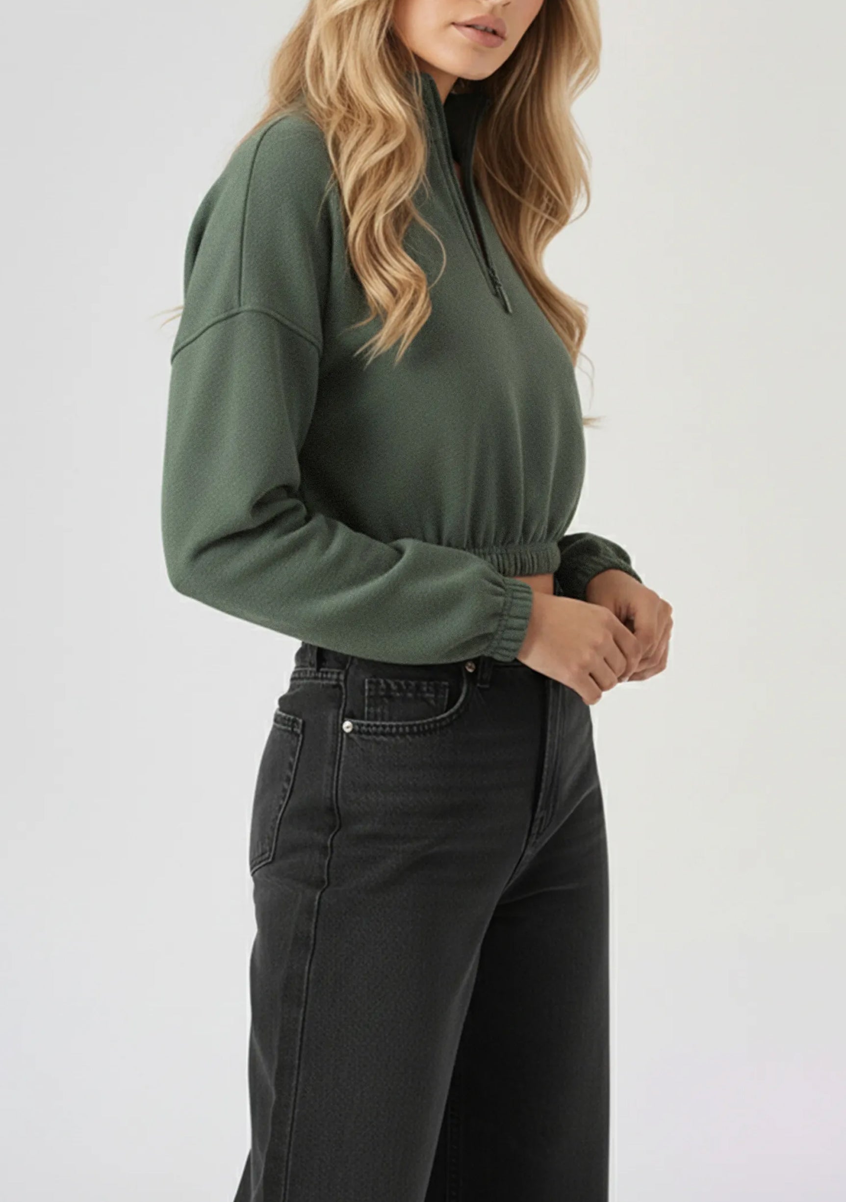 Side view of a model posing in a cropped green half zip sweatshirt