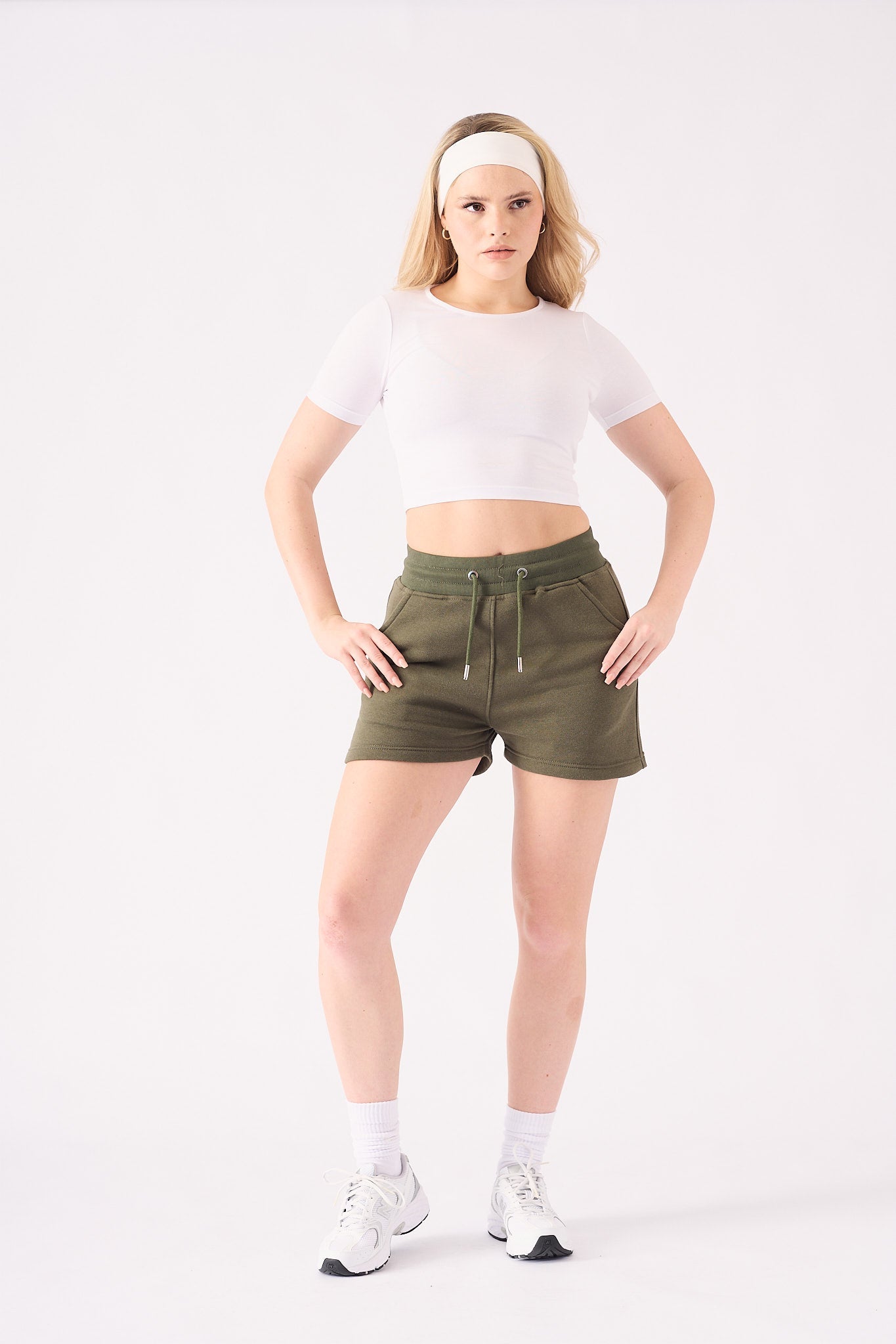 A front view of a woman wearing khaki green jogger shorts with a white crop top