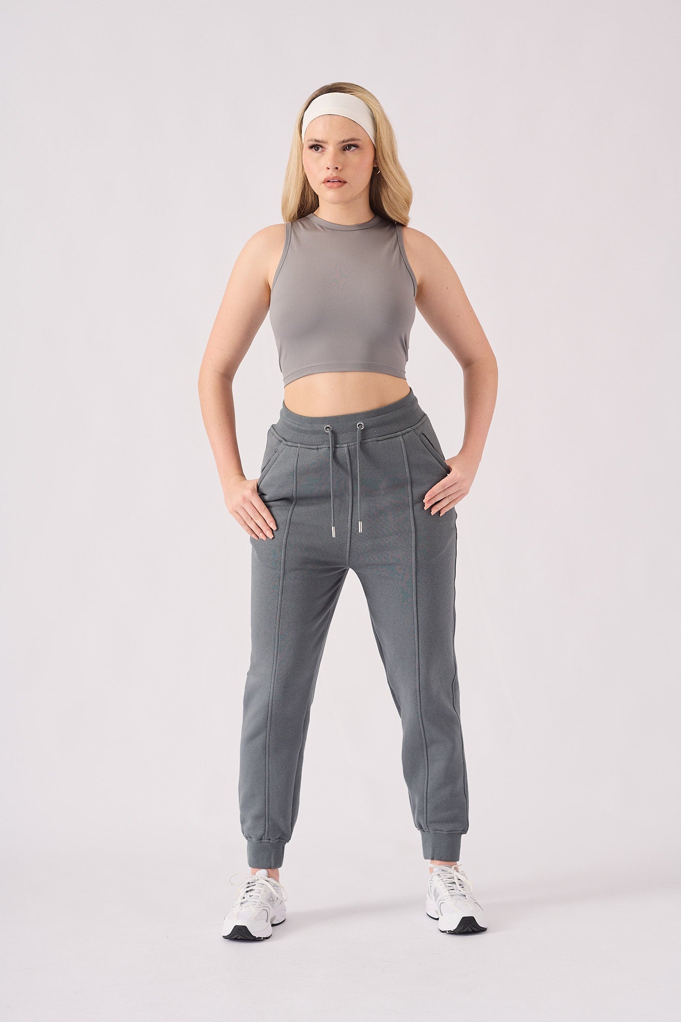 Full body shot of a woman in grey tapered joggers womens and a matching top.