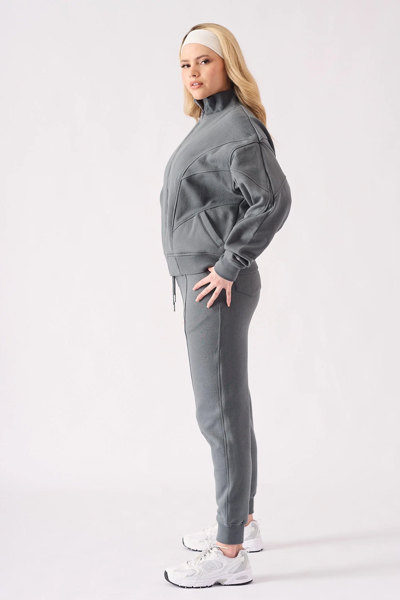 Full body side view of a model in a grey zip up hoodie and tracksuit set