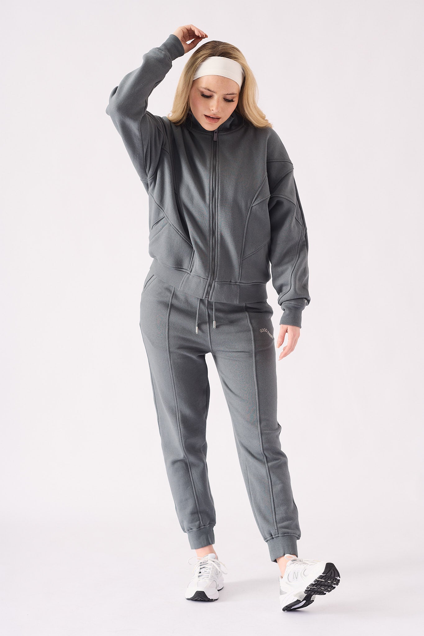 A model wearing a grey zip up hoodie with a white headband and matching joggers