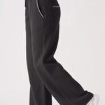 Side profile of the Herman black wide-leg joggers, showing the straight-leg silhouette and contrast stitch pocket.