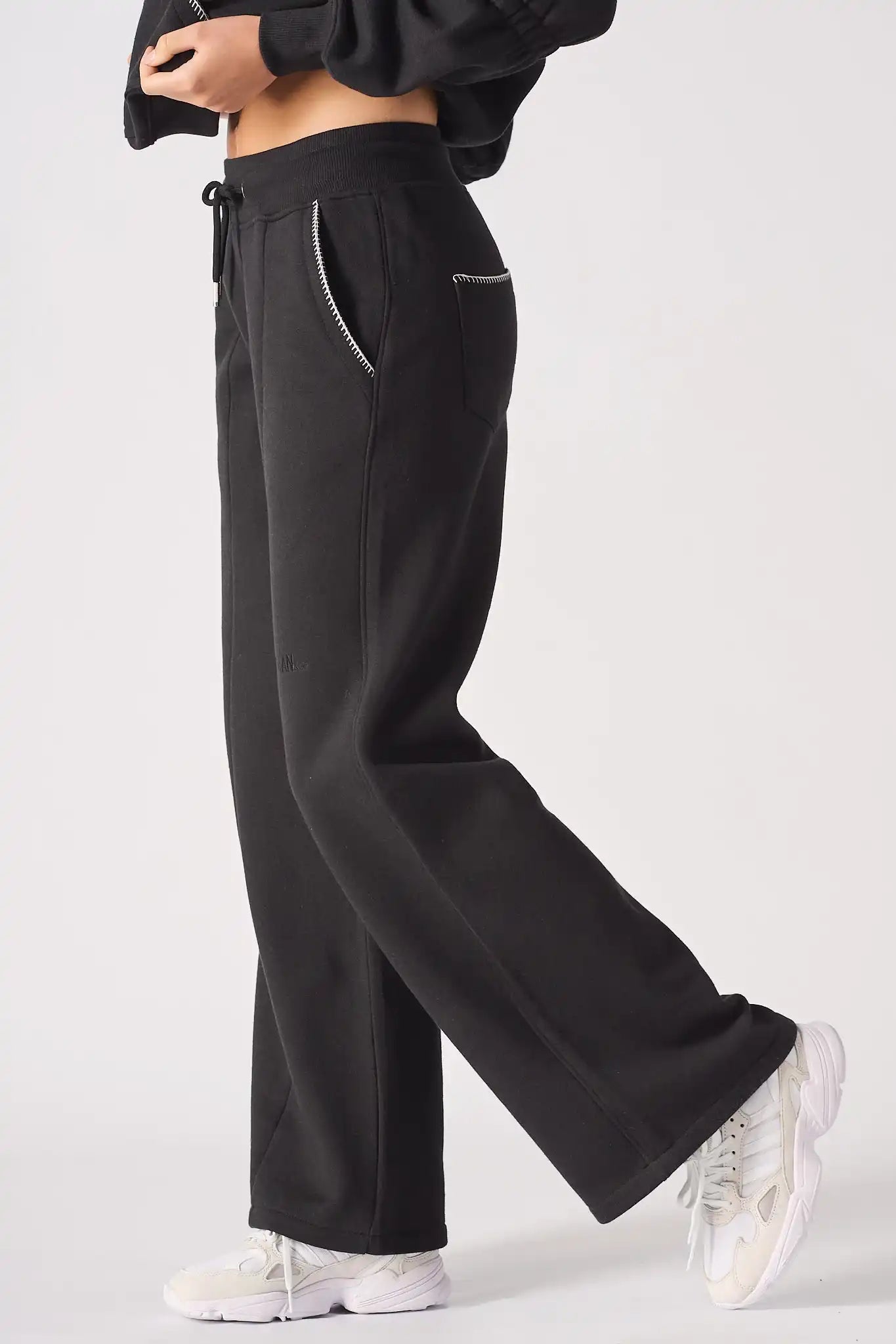 Side profile of the Herman black wide-leg joggers, showing the straight-leg silhouette and contrast stitch pocket.