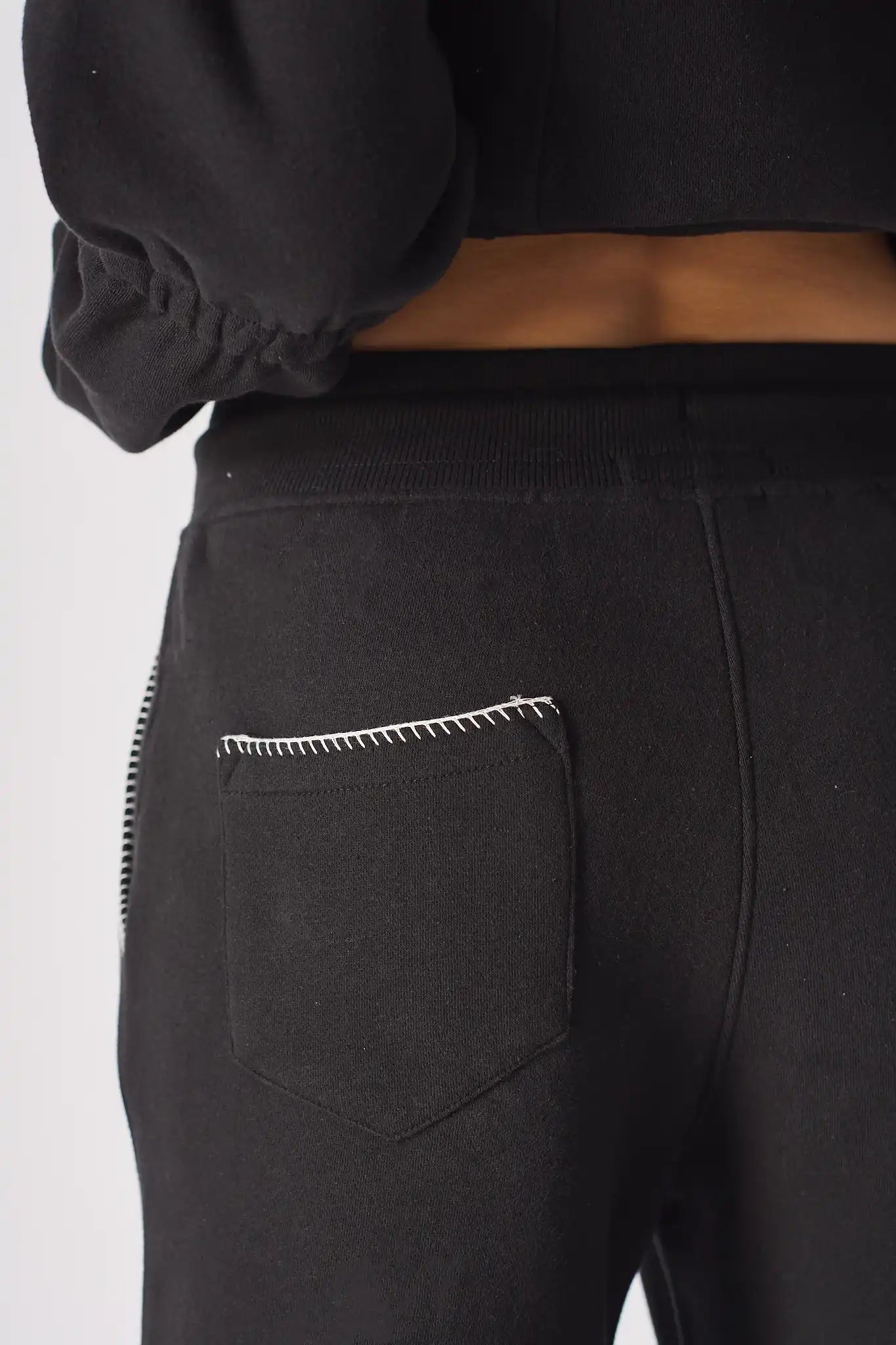 Detailed close-up of the contrast blanket stitch embroidery on the back patch pocket of the Herman black joggers.
