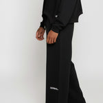 Close-up side view of the Herman men's black wide-leg joggers showing the logo detail.