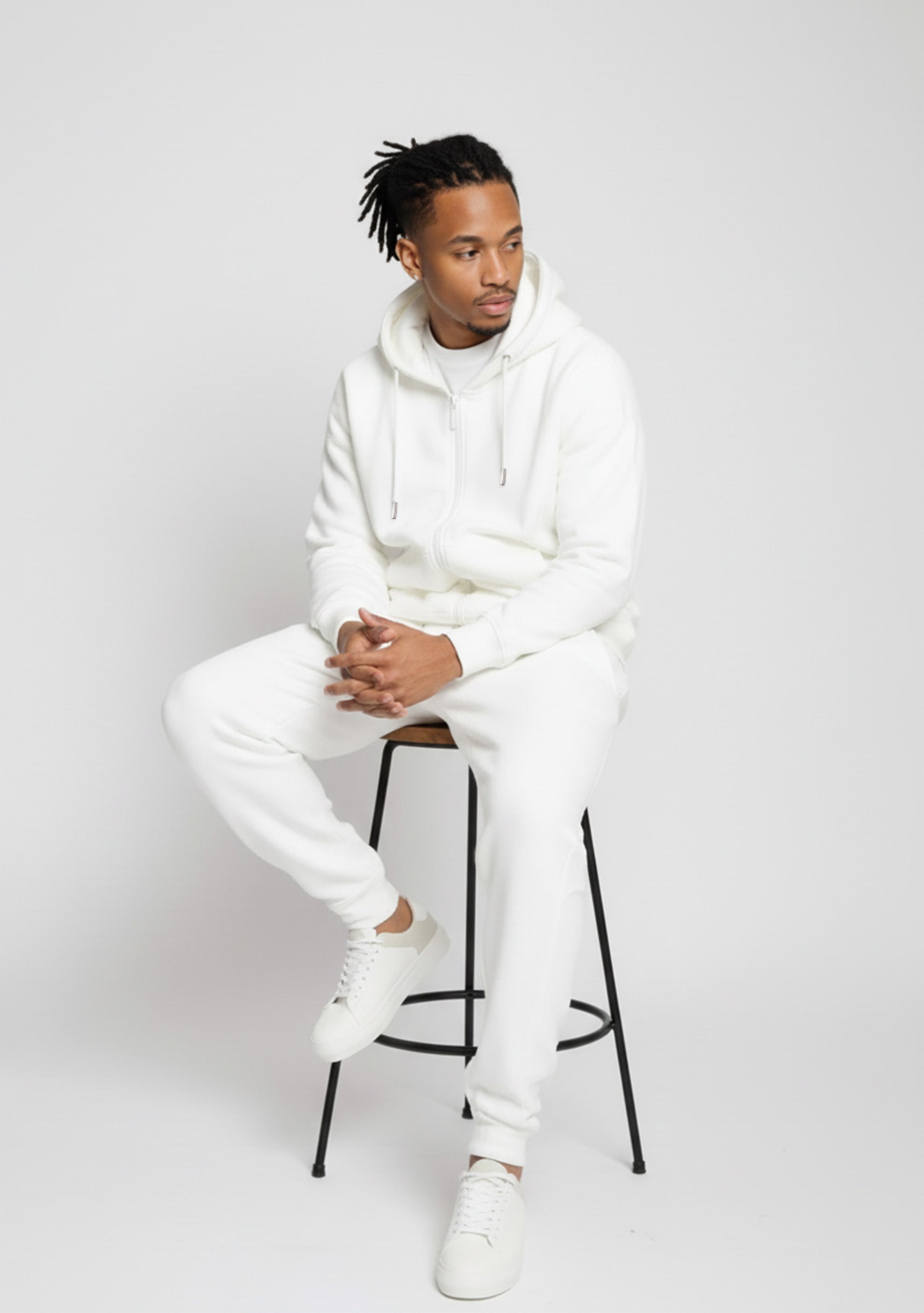 Model sitting while wearing the Herman men's white oversized zip hoodie and joggers set